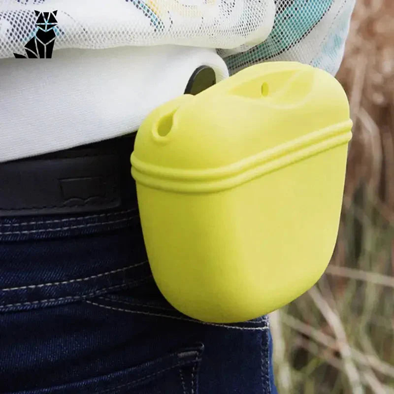 Femme tenant un étui jaune pour airpods avec un sac de dressage pour chien rempli de friandises pour le dressage